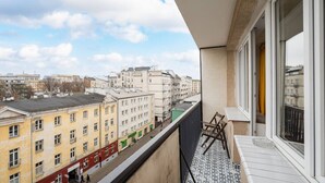 A balcony with a view of city buildings, a tiled floor, and a window with a curtain. - Wilcza Retro – City Center, Balcony – by Rentujemy (Warszawa)