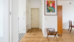 A hallway with a wooden floor, a white door, a framed poster on the wall, and a wooden cabinet. - Wilcza Retro – City Center, Balcony – by Rentujemy (Warszawa)