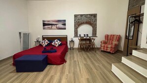 Habitació d'hotel amb un llit, una taula petita amb cadires, un butac armchair vermell, una llar de pedra i una escala.