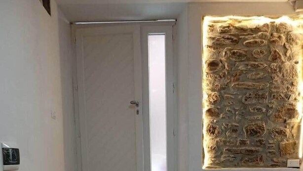 Gradi amb trams de fusta que condueixen a una porta, un mur de pedra amb il·luminació integrada i dos mobles d'emmagatzematge blancs.