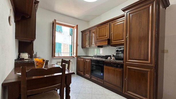 A kitchen with wooden cabinets, a dining table, chairs, a stove, and a window with shutters. - Il Grifo Apartment (Vernazza)