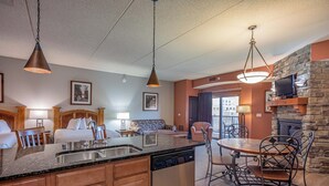 Een hotelkamer met een keukenhoek, een eettafel met stoelen, een open haard en een televisie.