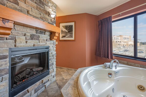 Un baño con chimenea de piedra, una bañera grande y un ventanal con vista a edificios.