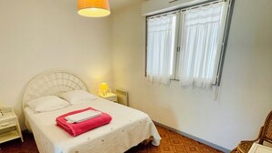 Hotellihuone, jossa on sänky, yöpöytä, lamppu, ikkuna verhoilla ja kuvioitu lattia.