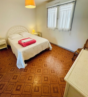 A hotel room with a bed, a nightstand, a lamp, a window with curtains, and a patterned floor.