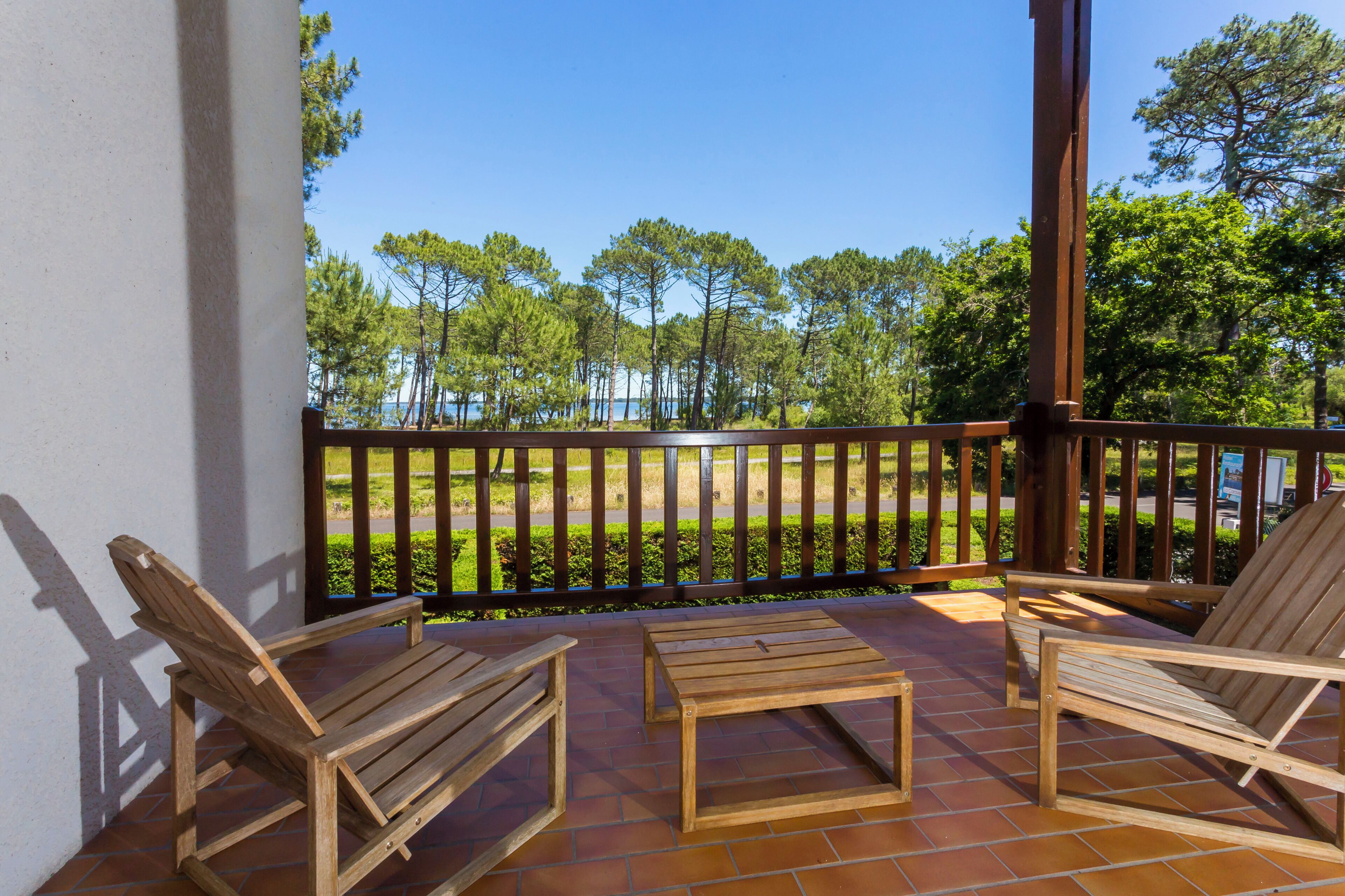 Eine Holzterrasse mit zwei Stühlen und einem Tisch, mit Blick auf eine angelegte Grünfläche mit Bäumen und einem Gewässer.
