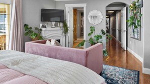 A bedroom with a bed, a pink ottoman, a TV, a fireplace, and a hallway with a plant. - Dream House - three bedroom, three in a half baths on Paschal Vineyard (Talent)