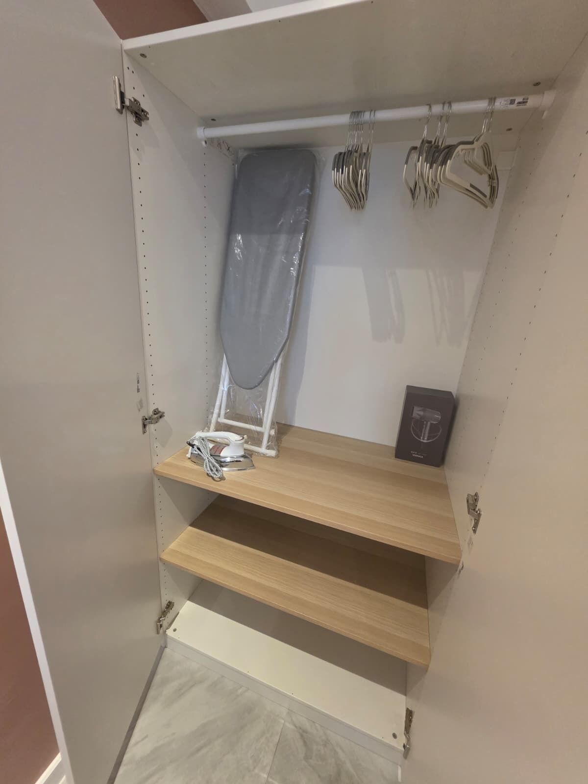 A storage unit with shelves, an ironing board, and hanging items.