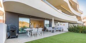 Un patio exterior moderno con una parrilla, zona de estar y césped bien cuidado.