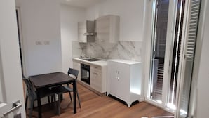 A compact kitchen with a dining table and chairs, a built-in oven, and a sliding glass door leading to a balcony. - Pigneto new collection 1 (Rome)