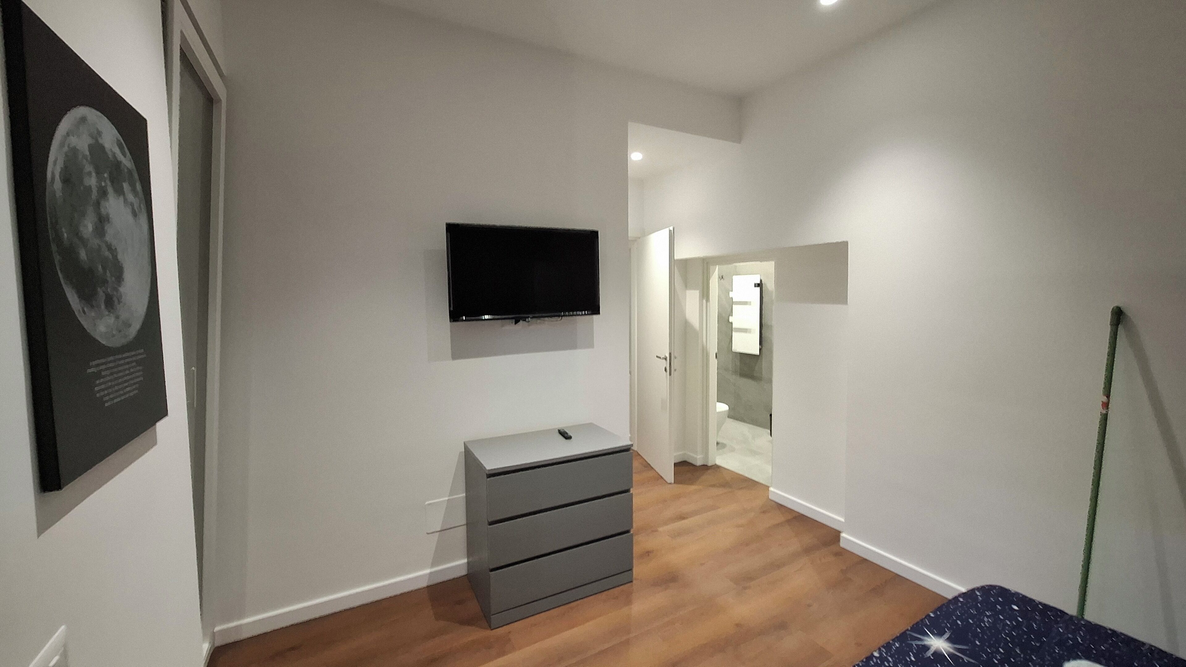 Un couloir avec un téléviseur à écran plat, une commode grise et une affiche accrochée au mur.