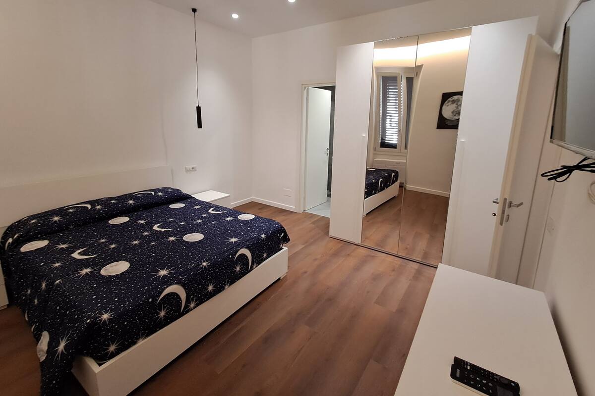 A bedroom with a bed, a wardrobe, a desk, and a mirror.