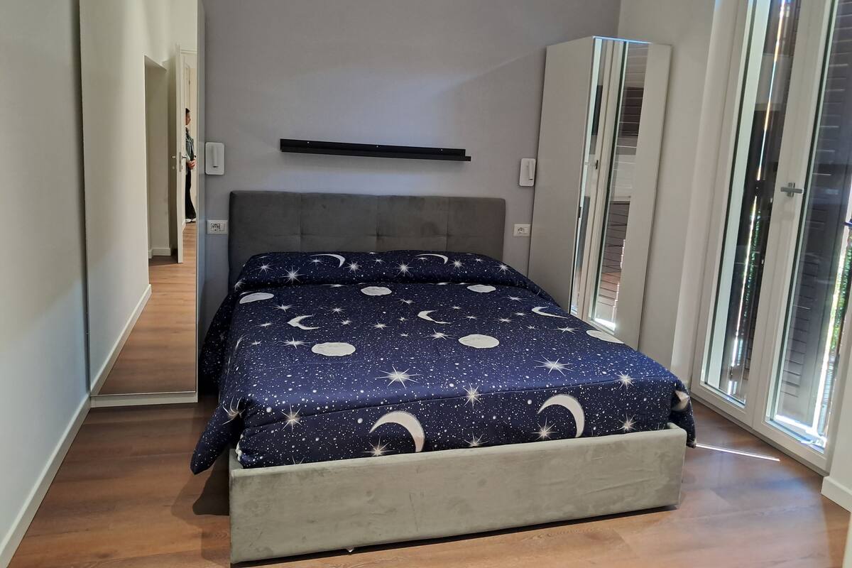 A bedroom with a bed, a wardrobe, a mirror, and a door leading to another room.