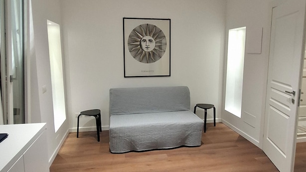 A room with a bed, a dining table, and a chair. There is a framed artwork on the wall and a door on the right. - Pigneto new collection 1 (Rome)