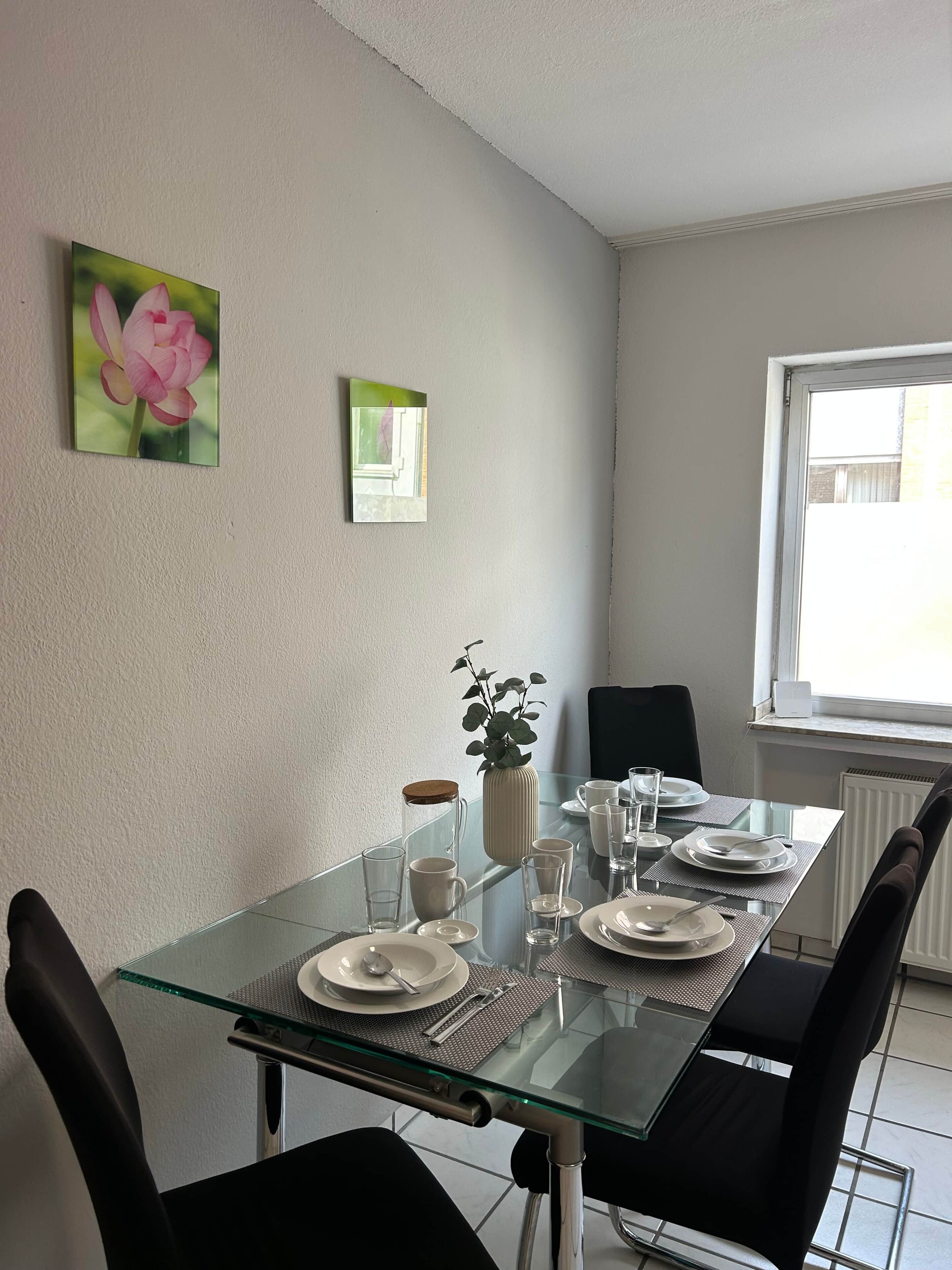 A dining area with a glass table, black chairs, a potted plant, and a window with a view.
