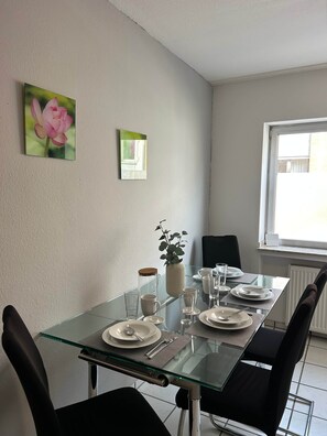 Uma sala de jantar com mesa de vidro, cadeiras pretas, uma planta em vaso e uma janela com vista.