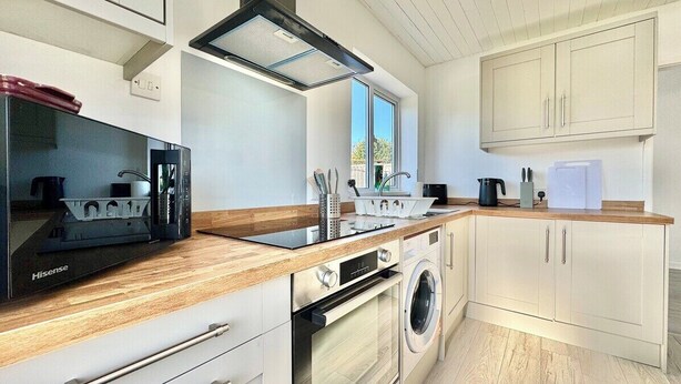 A modern kitchen with a microwave, oven, sink, and wooden countertop. - Modern 3 Bedroom Home | 4 Beds | Private Parking (Doncaster)