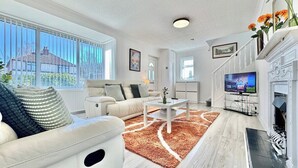 A living room with a sofa, coffee table, fireplace, TV, and large windows. - Modern 3 Bedroom Home | 4 Beds | Private Parking (Doncaster)