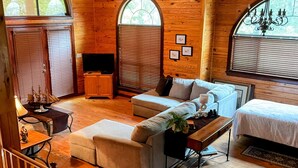 Un acogedor interior de cabaña con techo de madera, un sofá, una cama y una escalera.