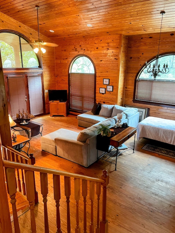 Un acogedor interior de cabaña con techo de madera, un sofá, una cama y una escalera.