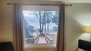 Et værelse med udsigt til en træterrasse, der fører ned til en strand, en stol med et blomstret pude og en lampe.