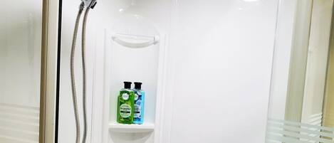 A shower with a handheld showerhead, a glass door, and two shelves with bottles.