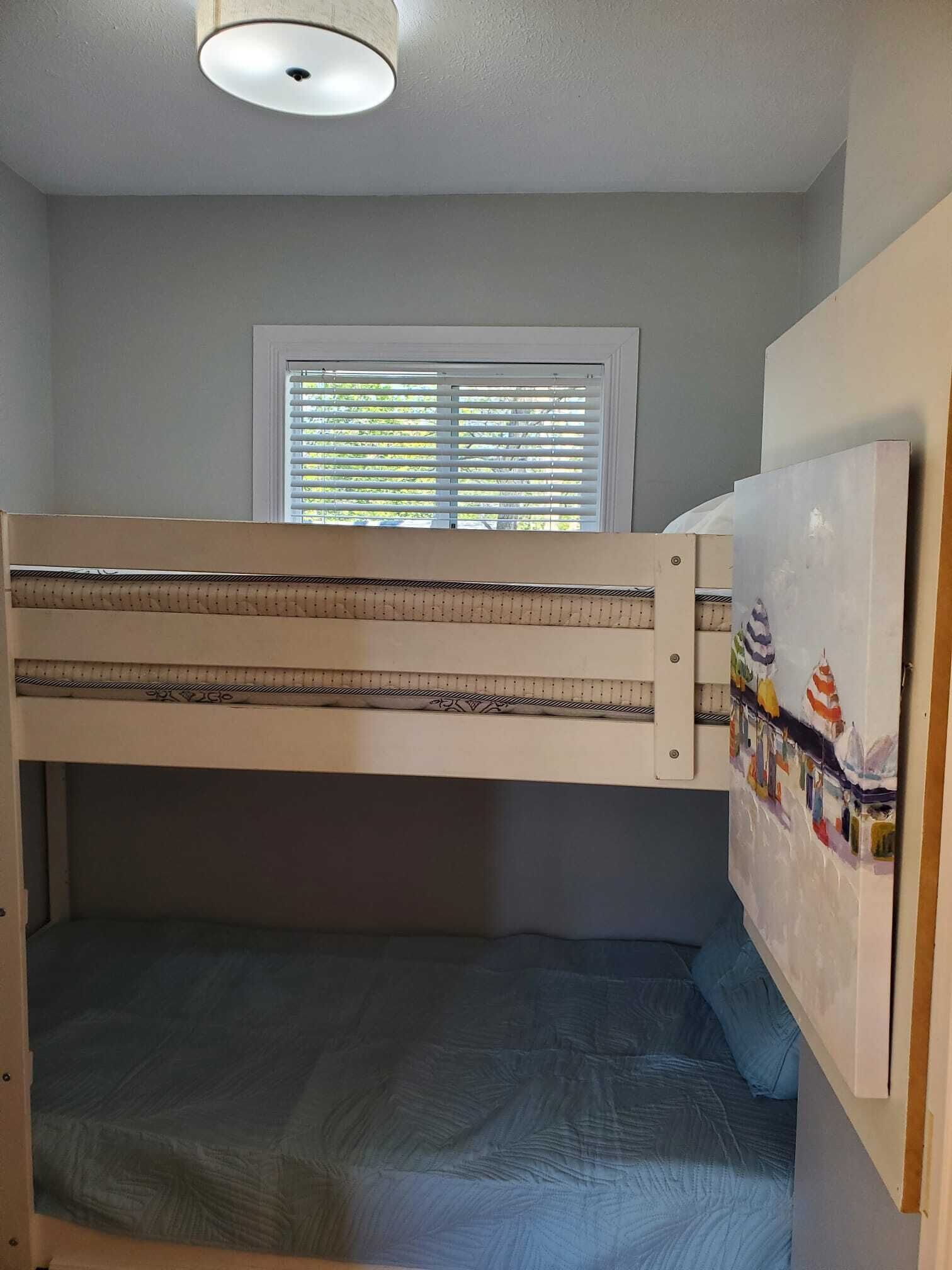 A bunk bed with a window above, a ceiling light, and a painting on the wall.