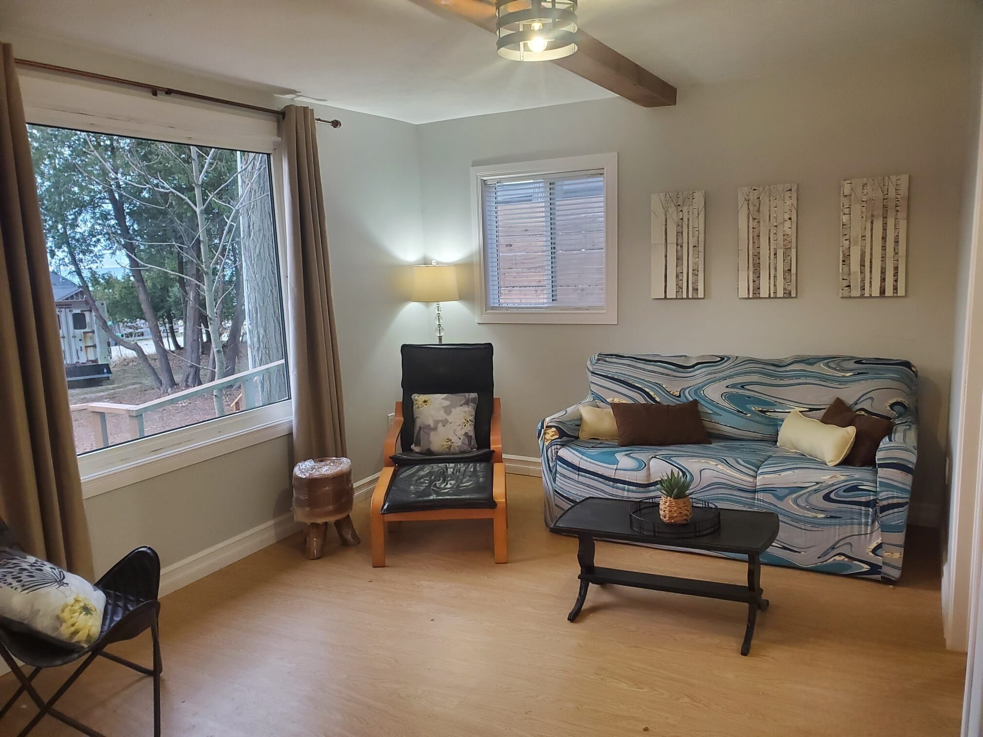 Una sala de estar con sofá, una silla, una mesa, una lámpara y una ventana con cortinas.