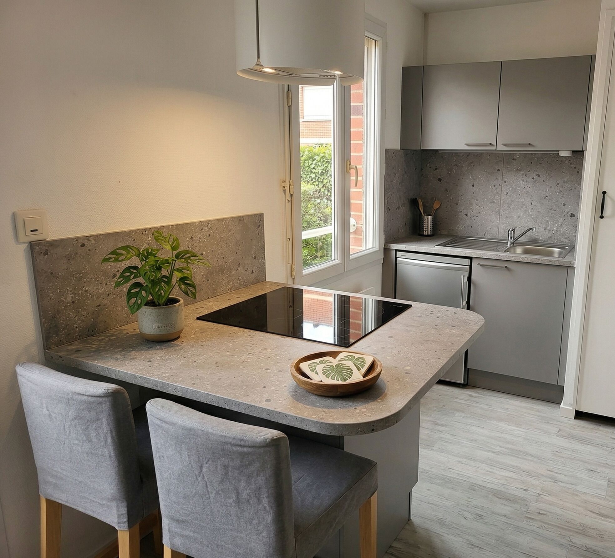 Una cocina moderna con una isla central, taburetes de bar, una planta en maceta y vistas al exterior.