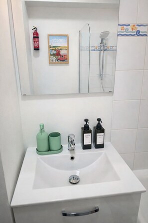 A bathroom with a white sink, green shampoo bottles, a silver faucet, and a framed picture above the mirror. - Le 28 : Studio - Terrace & Garden (Near Tram) (Valenciennes)