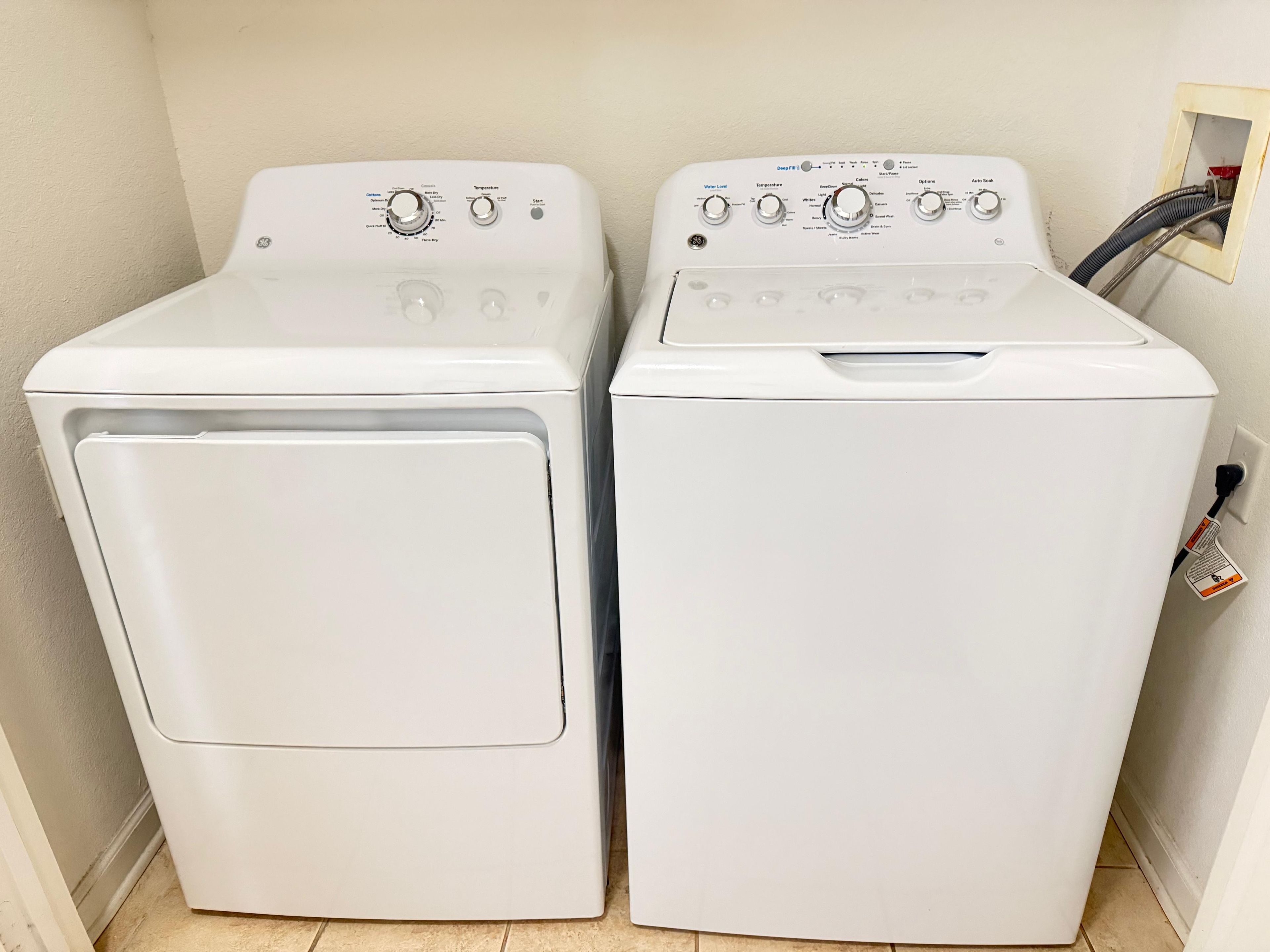 Deux machines à laver à chargement frontal, de couleur blanche, se trouvent dans une buanderie, avec une prise électrique fixée au mur.