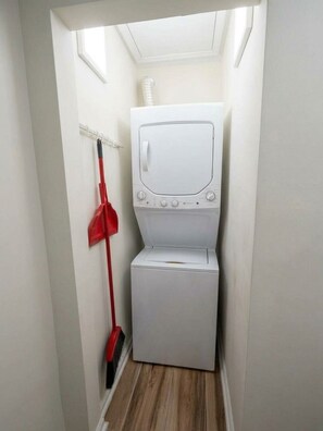 A laundry room with a washing machine and dryer, a broom, and a vent on the wall. - Charming House Retreat Near Charleston (Charleston)