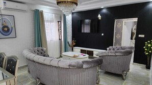 Ein Wohnzimmer mit einem runden Sofa, einem Couchtisch, einem an der Wand befestigten Fernseher und einer Deckenleuchte.