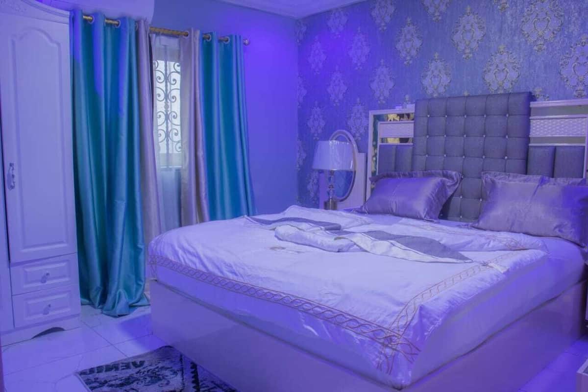 A bedroom with a large bed, a bedside table, a lamp, and a mirror.
