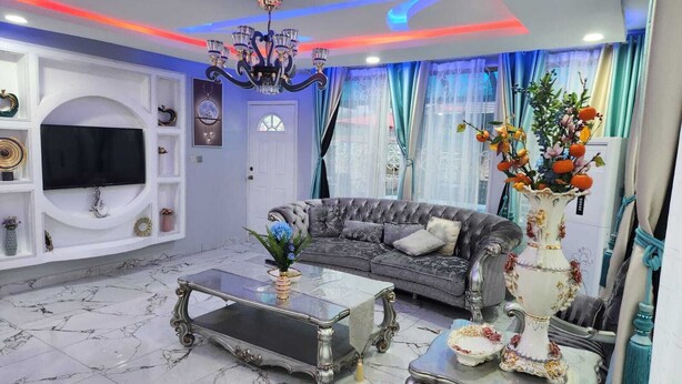 Ein Wohnzimmer mit einer Couch, einem Fernseher, einer Chandelieber und einer dekorativen Vase.