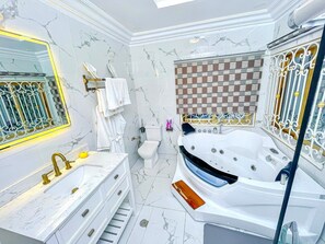 A bathroom with a marble wall, a large bathtub, a sink with gold fixtures, and a toilet.