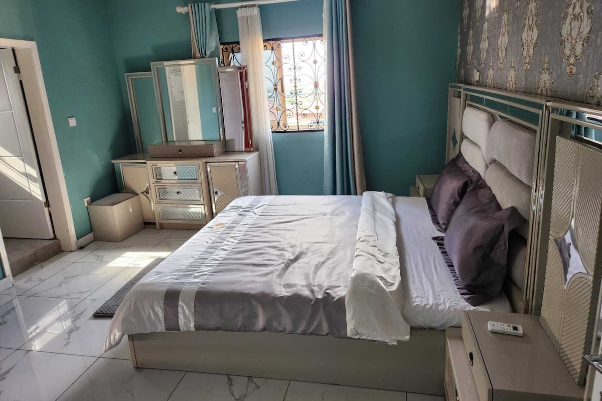 A bedroom with a bed, a dresser, a mirror, and a window with curtains.