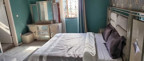 A bedroom with a bed, a dresser, a mirror, and a window with curtains.
