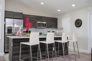 A modern kitchen with a central island, stainless steel appliances, and white bar stools. - Cozy Townhouse at Balmoral Resort (Haines City)