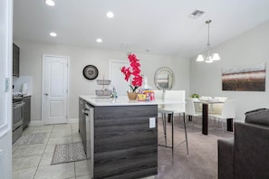 A modern kitchen with a dark wood island, white dining area with a round table, and a gray sofa. - Cozy Townhouse at Balmoral Resort (Haines City)