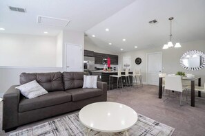 A modern living room with a sofa, a coffee table, and a dining area with chairs and a table. - Cozy Townhouse at Balmoral Resort (Haines City)