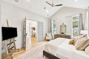 A bedroom with a bed, a TV on a stand, a ceiling fan, a window with curtains, and a door leading to another room. - Lakefront Home with Private Dock (Santa Rosa Beach)
