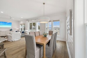 A spacious living room with a wooden dining table, grey upholstered chairs, a large window with a view, and a ceiling fan. - Pet-Friendly Beach Home with Private Pool, Lake Views, and Walk to Beach (Santa Rosa Beach)