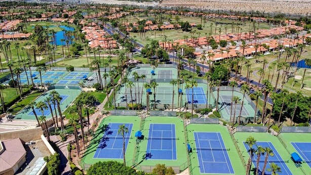 Vista aérea de una zona residencial con varias canchas de tenis rodeadas de palmeras y casas.