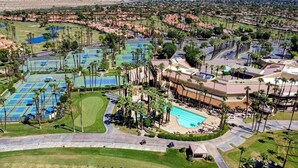 Vista aérea de un complejo turístico con varias canchas de tenis, una piscina y un campo de golf.