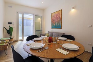 Zona pranzo con tavolo rotondo in legno apparecchiato per quattro persone, circondato da sedie nere. Sopra il tavolo, un quadro appeso al muro.