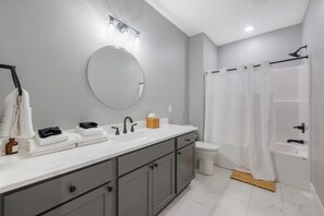 A modern bathroom with a large mirror, dual sinks, a toilet, and a shower area. - Family Home | Sleeps 8 | Walk to K-State (Manhattan)