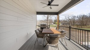 Une terrasse extérieure couverte, dotée d’une table et de chaises, d’un ventilateur de plafond et offrant une vue sur les environs.