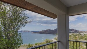 Uma varanda com vista para a paisagem costeira, incluindo um corpo de água e colinas ao longe.