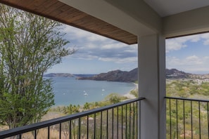 A balcony with a view of a coastal landscape, including a body of water and distant hills.
